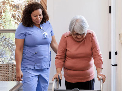 Physical therapist guiding an older woman in with a walker.