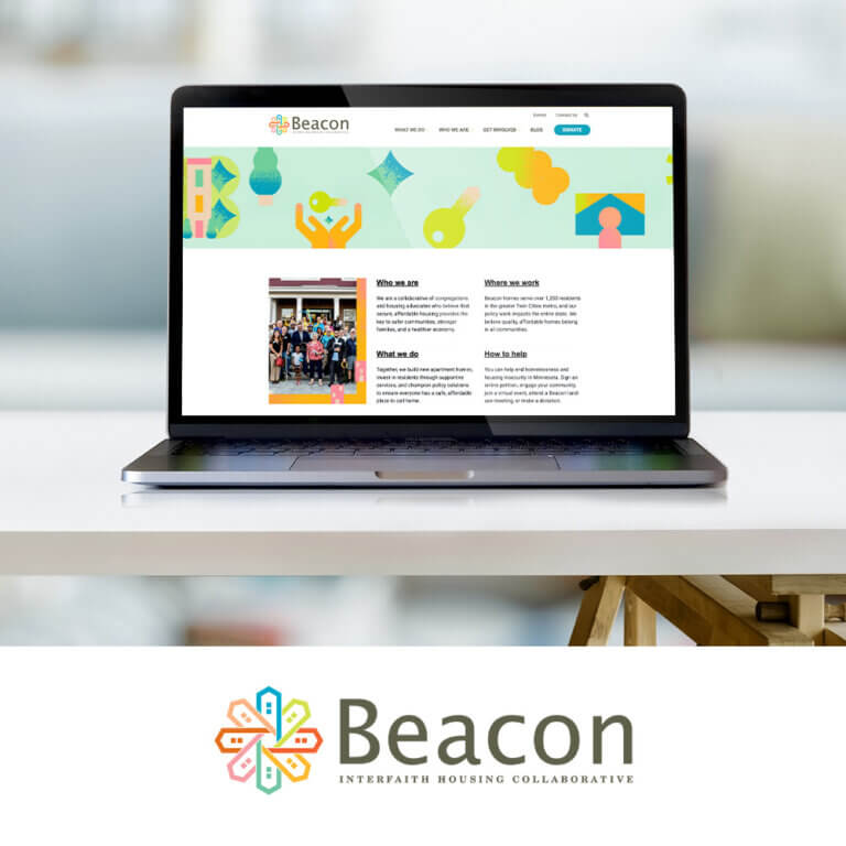 A laptop on a white desk displays the Beacon Interfaith Housing Collaborative website. The webpage features a colorful banner with abstract icons and sections titled Who we are, What we do, Where we work, and How to help, alongside a group photo of people gathered outside. Below the laptop is the Beacon logo, with a multicolored house-shaped flower icon and the text “Beacon Interfaith Housing Collaborative.”