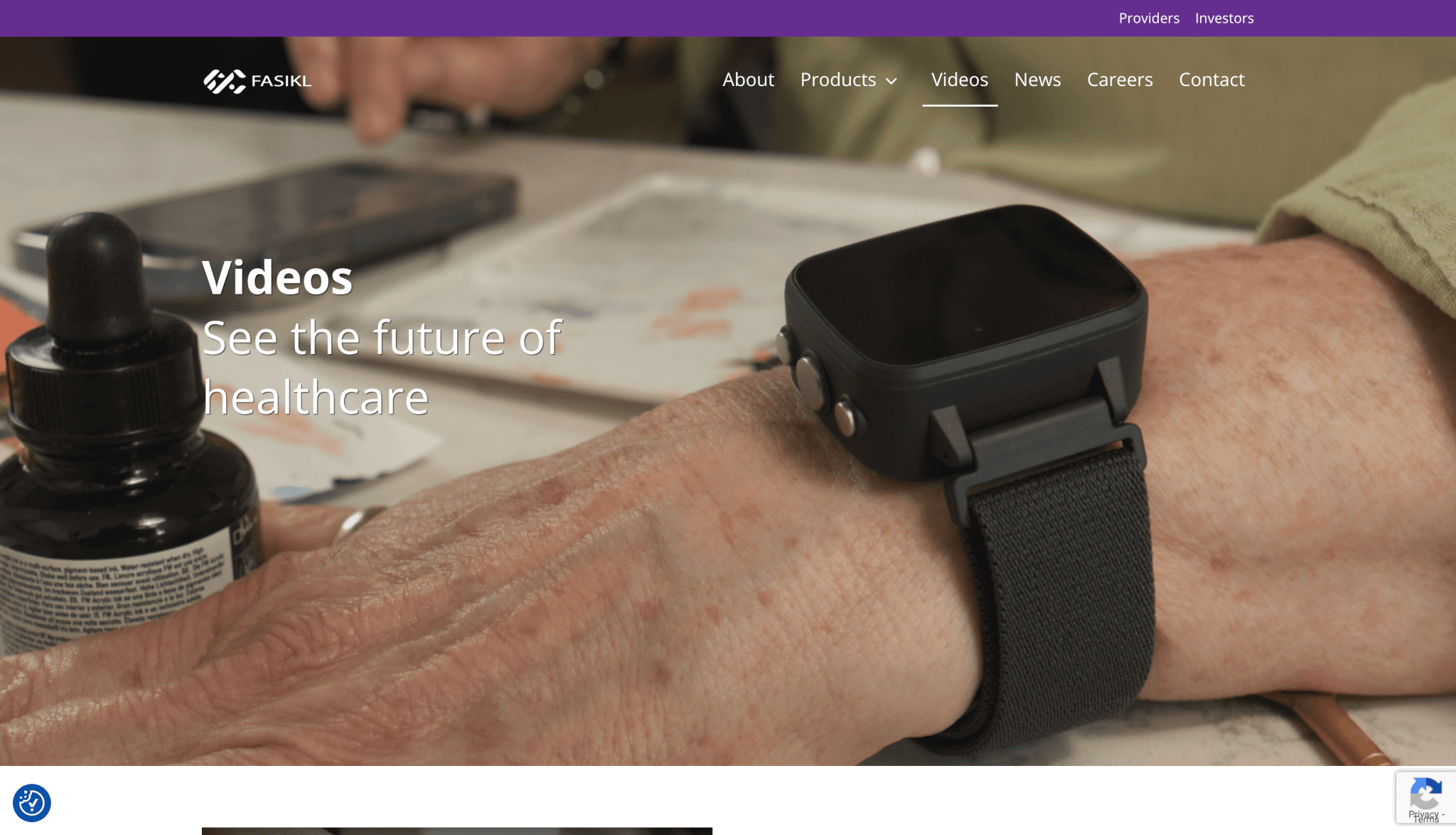 Fasikl website “Videos” page showing a close-up of an older person’s wrist wearing a sleek black smartwatch-style medical device beside a dark medicine dropper bottle and smartphone on a table. The page headline reads “Videos – See the future of healthcare,” with the Fasikl logo and navigation menu visible at the top on a purple header.