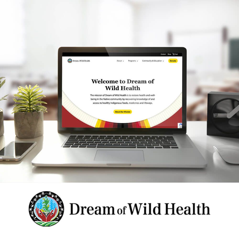 Laptop on a desk displaying the Dream of Wild Health website homepage, featuring the headline ‘Welcome to Dream of Wild Health,’ a mission statement about restoring health in Native communities, a yellow ‘About Our Mission’ button, and the Dream of Wild Health logo below.